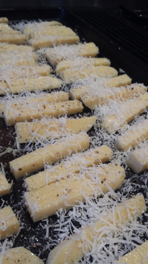 Polenta fries coated in olive oil, salt, pepper, and parmesan cheese, ready to go in the oven.